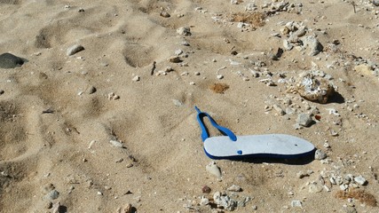 Fototapeta na wymiar One white broken slipper with blue strap left in the sand 
