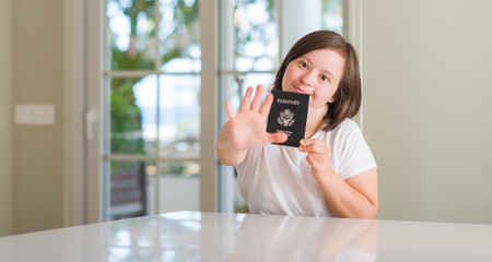 Down syndrome woman at home holding usa passport with open hand doing stop sign with serious and confident expression, defense gesture