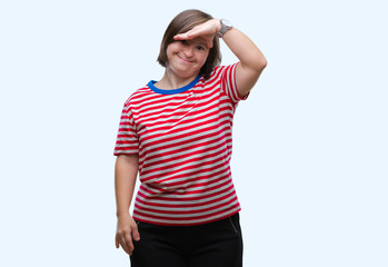Fototapeta premium Young adult woman with down syndrome over isolated background very happy and smiling looking far away with hand over head. Searching concept.