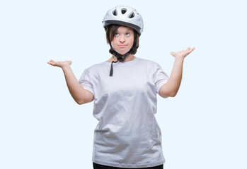 Young adult cyclist woman with down syndrome wearing safety helmet over isolated background clueless and confused expression with arms and hands raised. Doubt concept.