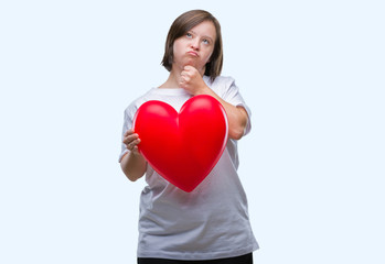 Fototapeta na wymiar Young adult woman with down syndrome holding red heart over isolated background serious face thinking about question, very confused idea