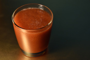 Glass of tomato juice on golden surface
