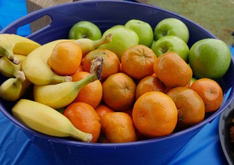 A tray of fresh tropical fruits including orange, apples, and ripe bananas