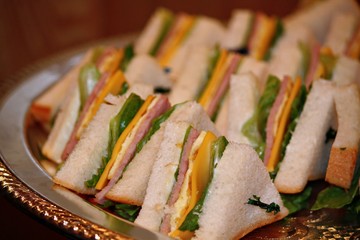 Sandwiches, sliced, arranged and served in a silver circular metal tray 