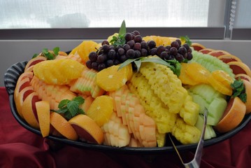Tropical fruit platter served in black circular tray with silver tongs