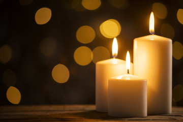 Three burning candles with blurred Christmas light