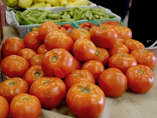 Big ripe tomatoes piled on a table with other fresh produce