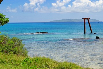 Fototapeta premium Beautiful seascape with an old relic from a shipwreck protruding in the crystal clear waters, with the Goat Island seen in the distance.