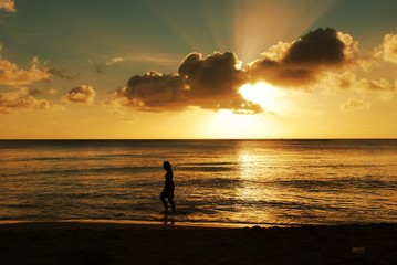 Silhouette of a woman walking away from the beach at sunset, with gorgeous clouds and streaks of the setting sun in the skies