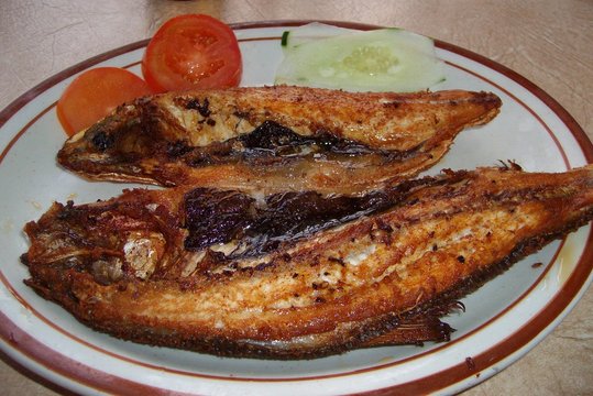 Crispy fried milk fish or bangus served with cucumbers and tomatoes in a round white plate with red borders