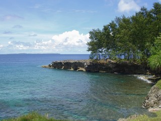 Clear blue and green waters with small coral formations and cliffs at a tropical beach 