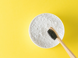 A jar of tooth powder and a wooden brush on a yellow background.