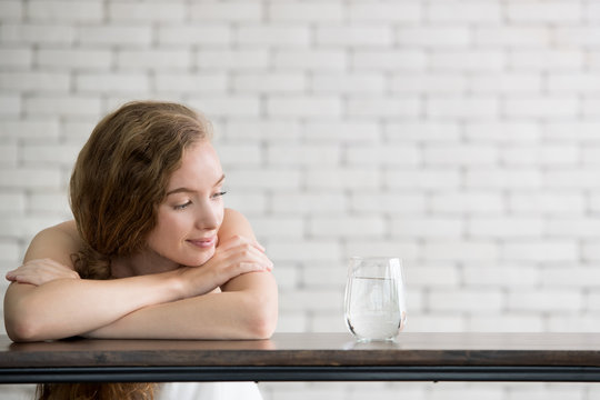 Beautiful young woman in joyful postures with jug and glass of drinking water on the side