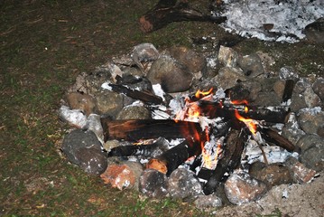 burning embers from a bonfire in the ground, surrounded by stones