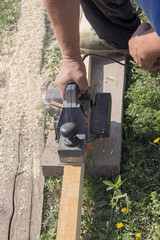 The carpenter works with an electric planer on a wooden Board on the street