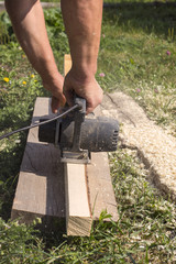 The carpenter works with an electric planer on a wooden Board on the street