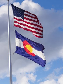 Close up photo of the flag of the United States of America and Colorado State flag waving in the wind from one pole
