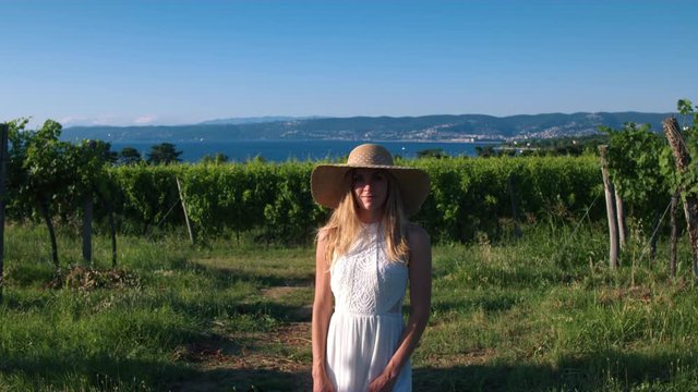 Portrait - Young woman in white dress and a sun hat standing in the vineyard - Powered by Adobe