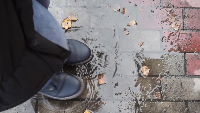 Legs in dark blue boots stand in a puddle and the grass stomp in the water, so that the spray fly in different directions, fall on his feet leaves
