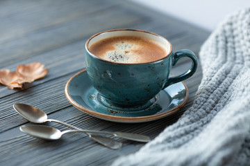 Blue cup whith coffee, knitted sweater, autumn leaves on wooden background. Cozy morning.