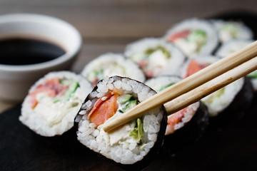 Eating sushi. Food photo, Japanese restaurant, dinner. Pair of chopsticks taking sushi roll from plate, close up