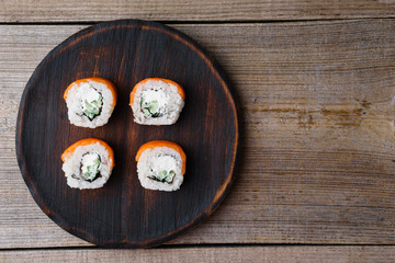 Japanese cuisine, food background. Tasty appetizing sushi rolls with salmon served on wooden plate, flat lay with copy space