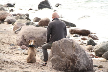 Mann mit Hund  sitzt am Strand