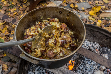 Preparation of pilaf on an open fire. Mixing of meat and onions. A pan with pilaf on the fire. Autumn in Siberia