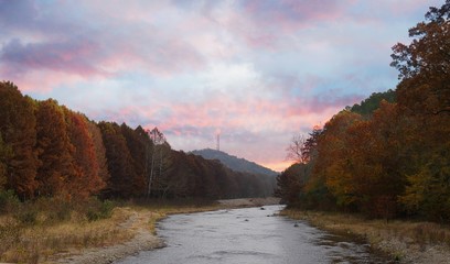The tranquil Mountain Fork River flowing at the Beavers Bend State Park in Broken Bow, Oklahoma with colorful leaves on the trees on a beautiful autumn day.