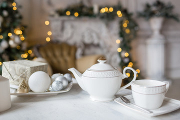 Tea time, white teapot and cups on the table. Decorated Christmas tree. Classic apartments with a...