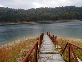Wide scenic shot of a lake with a wooden bridge and colorful leaves in the trees in a state park on a beautiful autumn day.