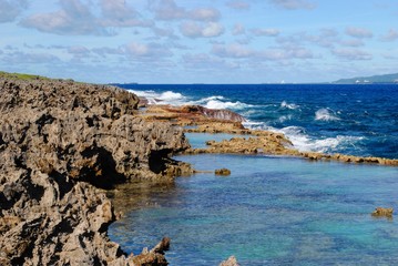 Sharp rocky shorelines with clear blue waters of the Tinian channel and a view of Saipan island in the far distance 