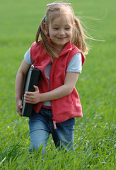 Little girl with a laptop on green field