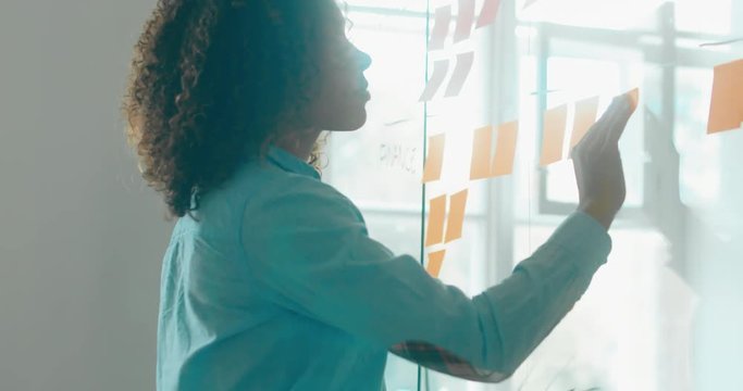 African American black employee looking onto a glass wall with sticky notes, framework for managing work, scrum methodology. 4K UHD 60 FPS SLOW MOTION