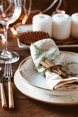 Thanksgiving table setting among white candles and cones. Ceramic plate with fork and knife on a linen napkin. Close up.