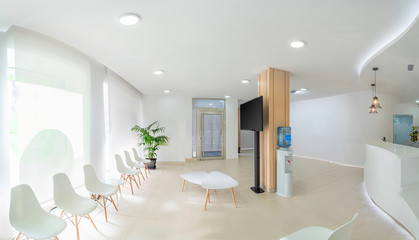 Panorama of a bright reception and waiting room in a clinic with desk, modern chairs and plants....