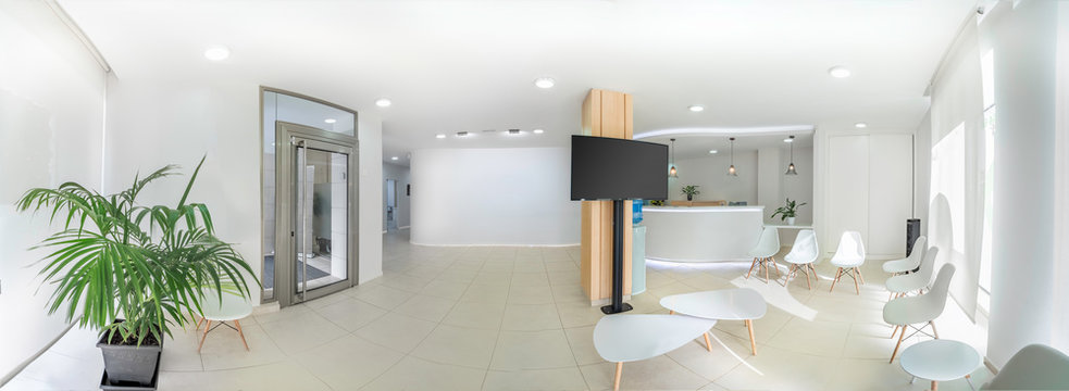 Panorama of a bright reception and waiting room in a clinic with desk, modern chairs and plants. Indoor mockup with screen with copy space.