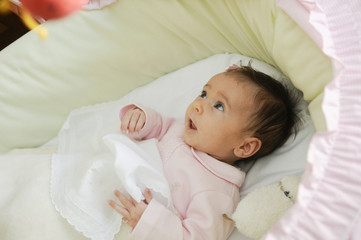 Baby girl looking at a doll in his crib