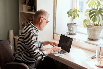 Senior man at home in front of laptop computer working. Freelancer, on line worker