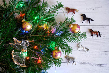 Decorated with toys and lights, the branch of the Christmas tree next to horses and an angel