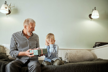 generation, christmas. grandfather and grandson with gift box sitting on couch at home