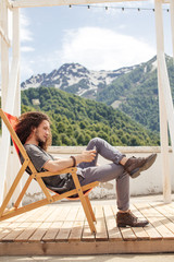 man sitting in chair using phone with mountains on background
