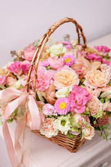 Fototapeta na wymiar flowers arrangement with various of colors in wicker basket on pink table. beautiful spring bouquet. bright room, white wall. copy space