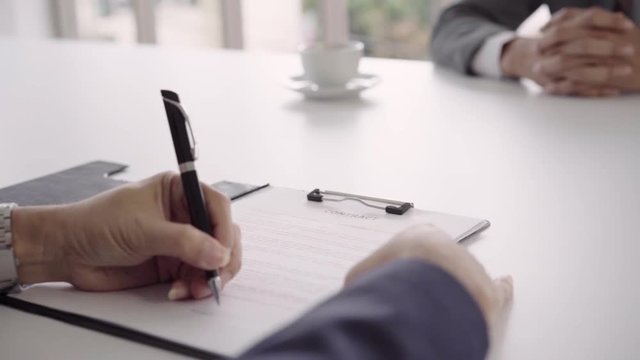 Slow motion - Smart handsome businessmen meeting in workplace with his colleague and signing a contract, recruitment and agreement concept. Male making a deal.