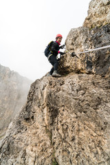 young attractive female mountain climber on a steep and exposed Via Ferrata in Alta Badia in the...