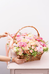 Women's hands touch flowers arrangement with various of colors in wicker basket on pink table. beautiful spring bouquet. bright room, white wall. copy space