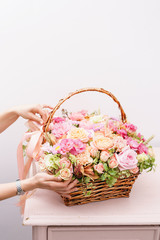 Fototapeta na wymiar Women's hands touch flowers arrangement with various of colors in wicker basket on pink table. beautiful spring bouquet. bright room, white wall. copy space