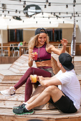 Sportive man and attractive blond woman in tracksuit sitting in outdoor cafe in summer morning with two glasses of drinks