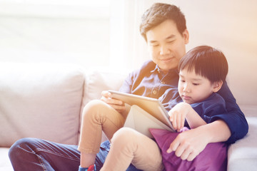Fototapeta premium Asian boy is watching a tablet. father taught social learning from around the world to his son. Or what the children do not understand. It is a good family relationship. Father's Day Family concept