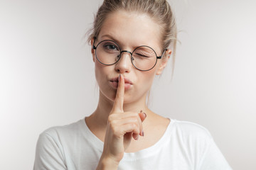 Finger on lips - silent gesture. Caucasian young woman in round spectacles holding her finger to...